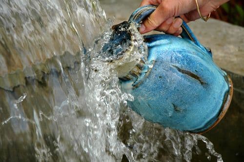 alt-Main tenant une cruche pour la remplir dans une fontaine